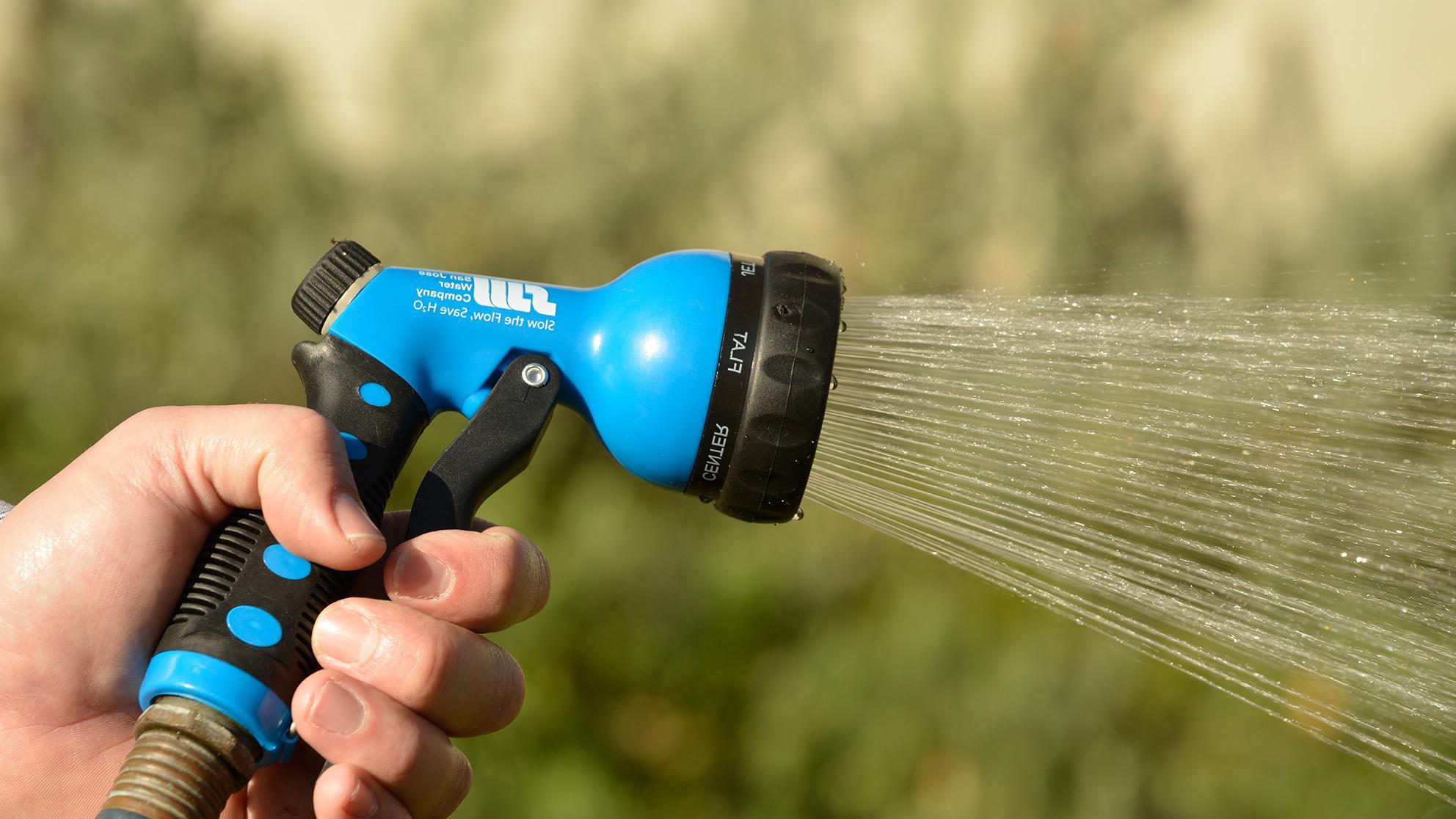 Hand holding a garden hose with blue nozzle spraying water